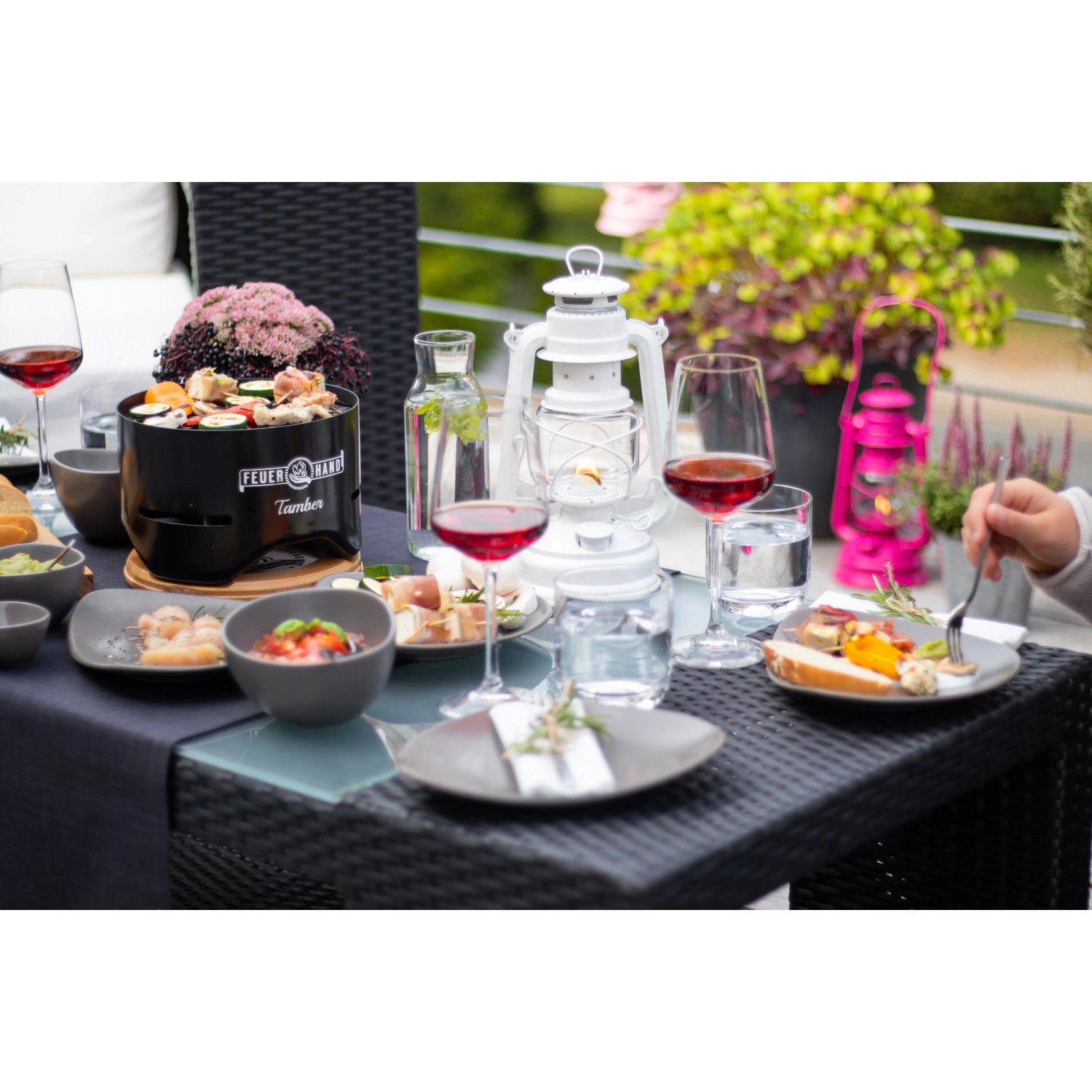 Feuerhand Tischgrill Tamber, tiefschwarz, mit Speisen und Getränken auf einem Tisch.
