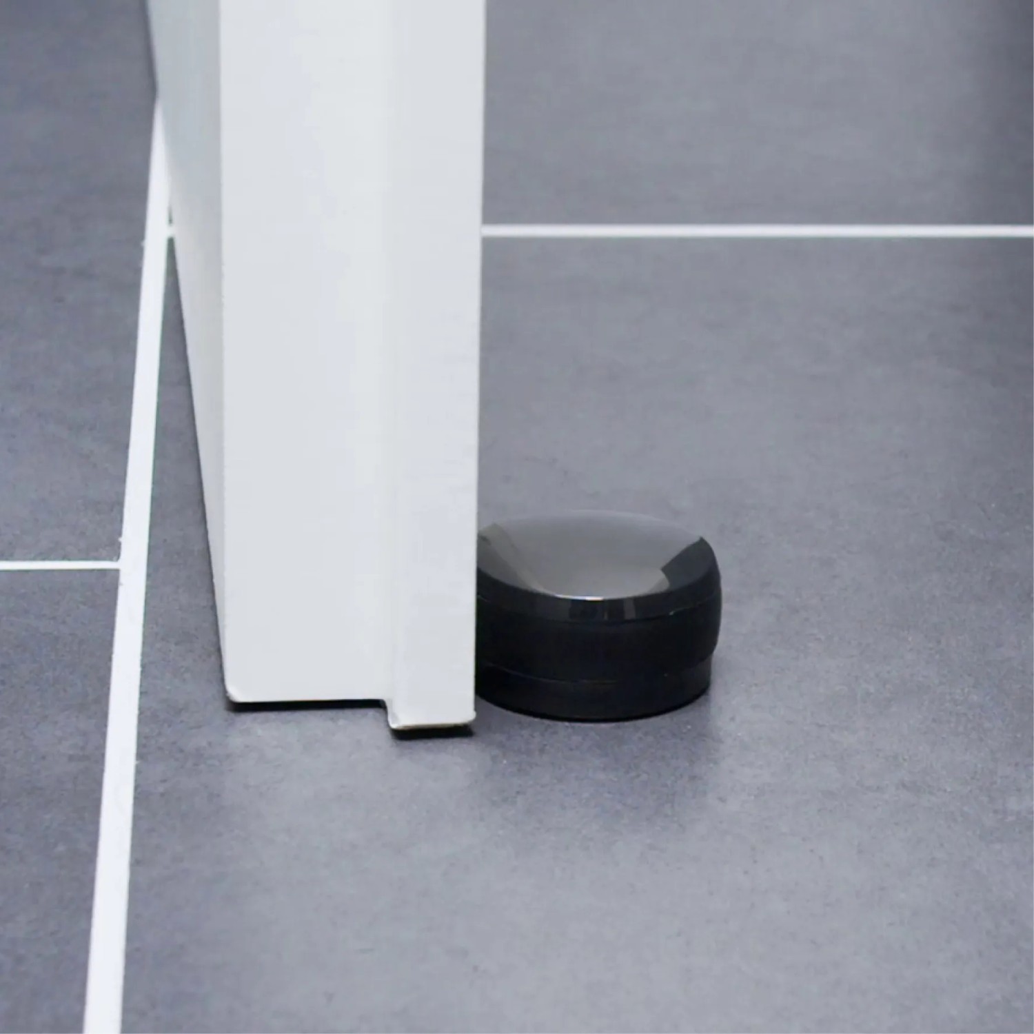 Schwarzer Wagner Bodentürstopper Black Deluxe aus Kunststoff, selbstklebend, neben einer Tür auf Fliesen.