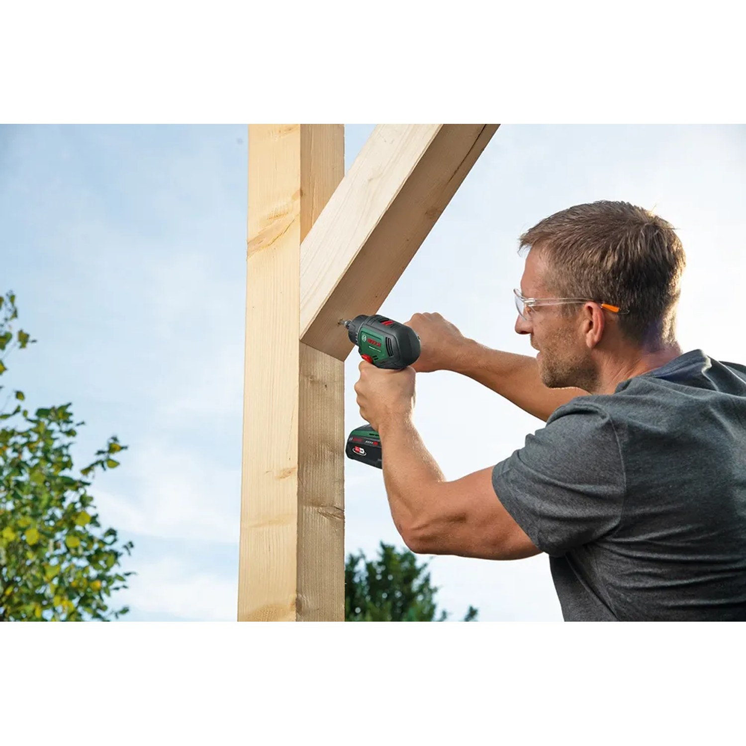 Mann schraubt mit dem Bosch 18V Akku-Bohrschrauber Advanced Drill 18 V-80 ein Holzkonstrukt zusammen.