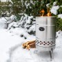 Feuerhand Pyron Feuertonne aus Edelstahl (25 l) im Schnee mit brennendem Holz. Grillutensil für Lagerfeuer.