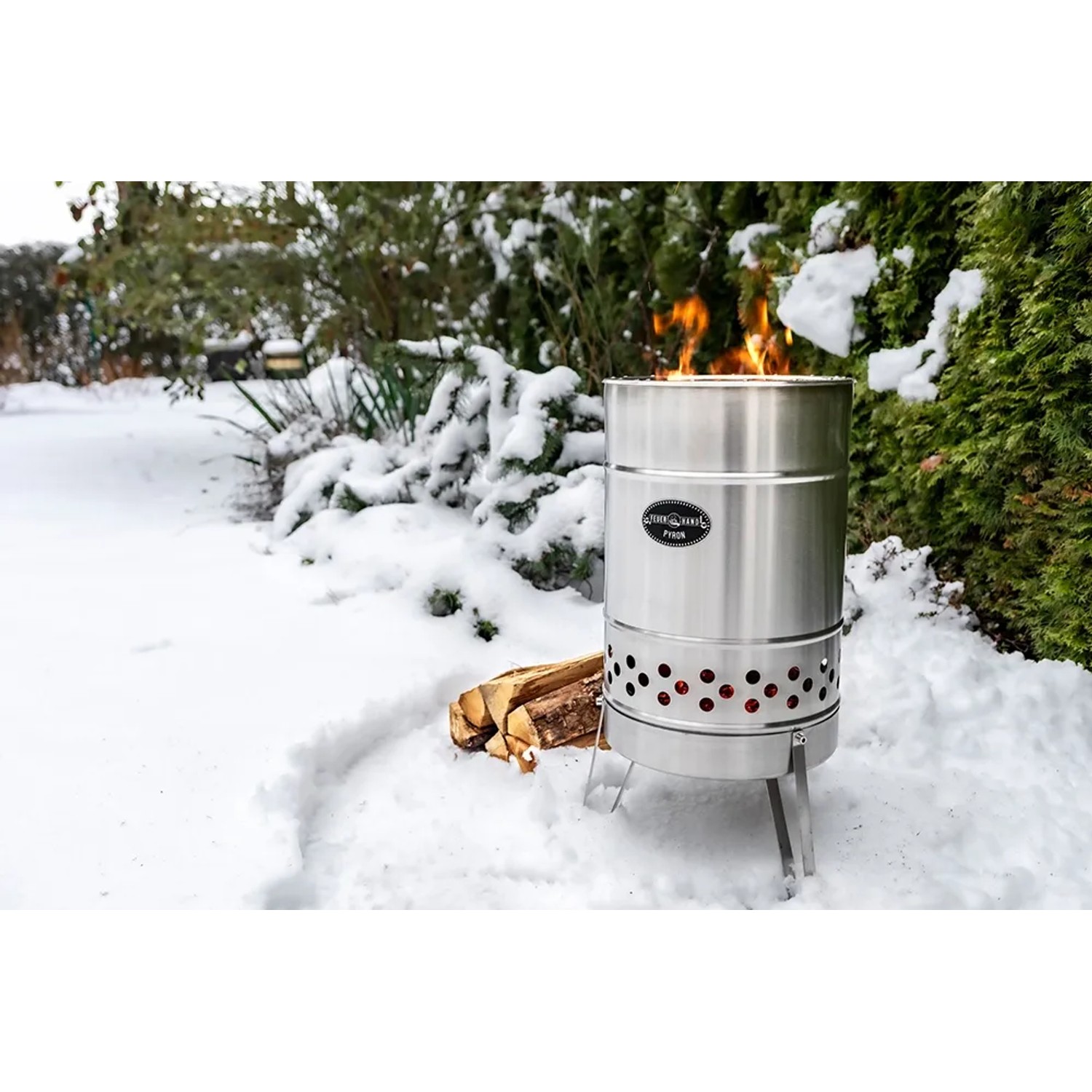 Feuerhand Pyron Feuertonne aus Edelstahl (25 l) im Schnee mit brennendem Holz. Grillutensil für Lagerfeuer.