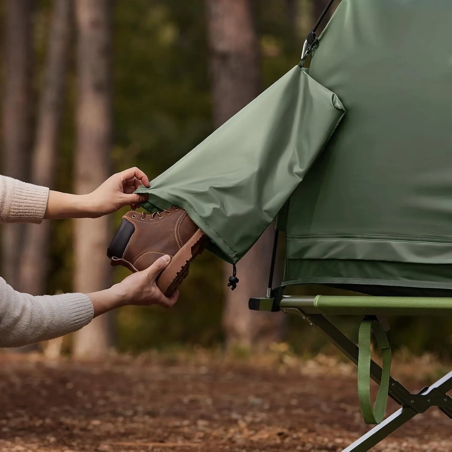 Person verstaut braunen Schuh in grüner Seitentasche des SoBuy Campingzeltes mit Feldbett. Praktisches Outdoor Zubehör.