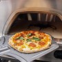 Buschbeck Pizzaofen X1 mit Pizza auf Schieber vor dem Ofen. Holzkohlegrill mit Gasbetrieb.
