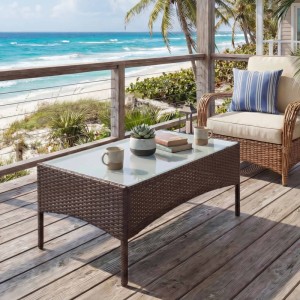 Brauner Poly-Rattan Gartentisch Hamar mit Glasplatte auf Holzterrasse am Meer. Ideal als Beistelltisch.