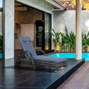 Graue Polyrattan Sonnenliege mit blauer Polsterung und Rollen auf dunkler Terrasse am Pool. Verstellbare Gartenliege.