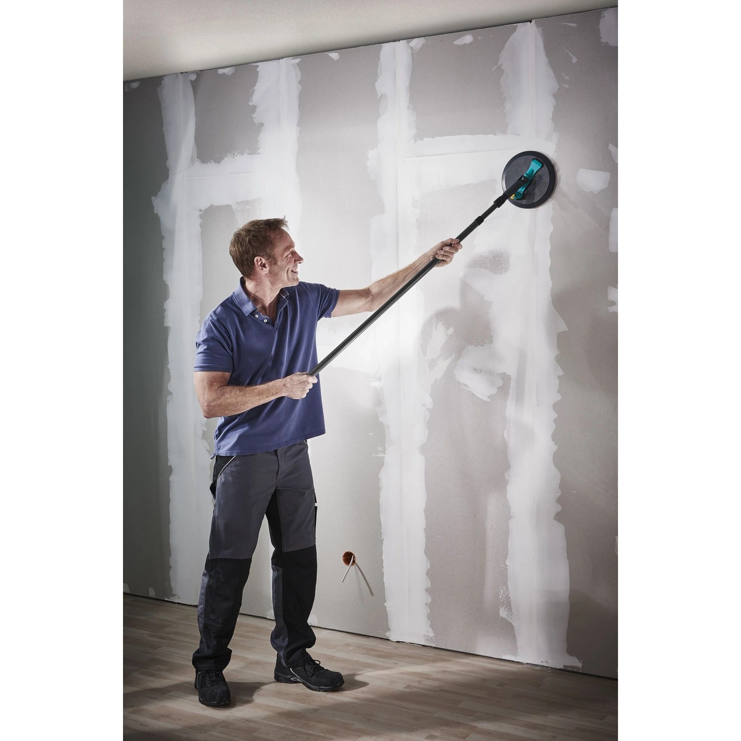 Mann schleift Trockenbauwand mit wolfcraft Rundschleifer Ø 225 mm und Teleskopstiel. Effizientes Werkzeug für Wände.