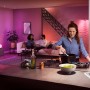 Szene mit Philips Hue E14 LED Lampe: Frau kocht, Wohnbereich mit farbiger Beleuchtung.