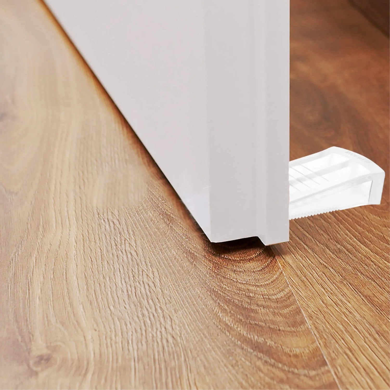 Transparenter Wagner Türkeil Standard unter einer Tür auf Holzboden. Türstopper aus Kunststoff, 80x30x15 mm.