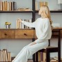 Blonde Frau in weißem Pullover wählt ein Buch aus einem Holzregal. Perfekt für Buchstützen aus Bambus und Edelstahl im Büro.
