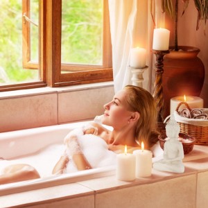 Frau entspannt in Badewanne mit weißer Buddha Figur aus Keramik und Kerzen im Bad.