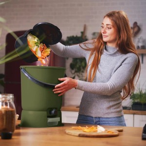 Frau befüllt Skaza Bokashi Komposter (olivegrün) mit Küchenabfällen. Starterset mit Zubehör.