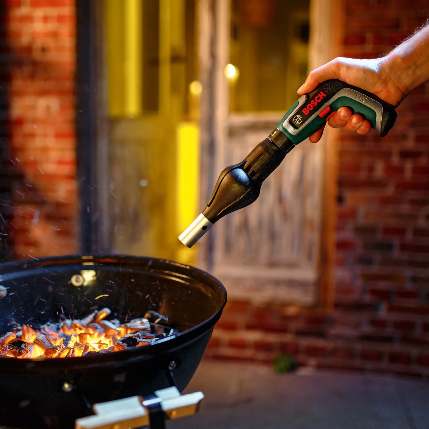 Bosch IXO 7 Akkuschrauber-Set mit Grillanzünder-Aufsatz im Einsatz über einem Holzkohlegrill.