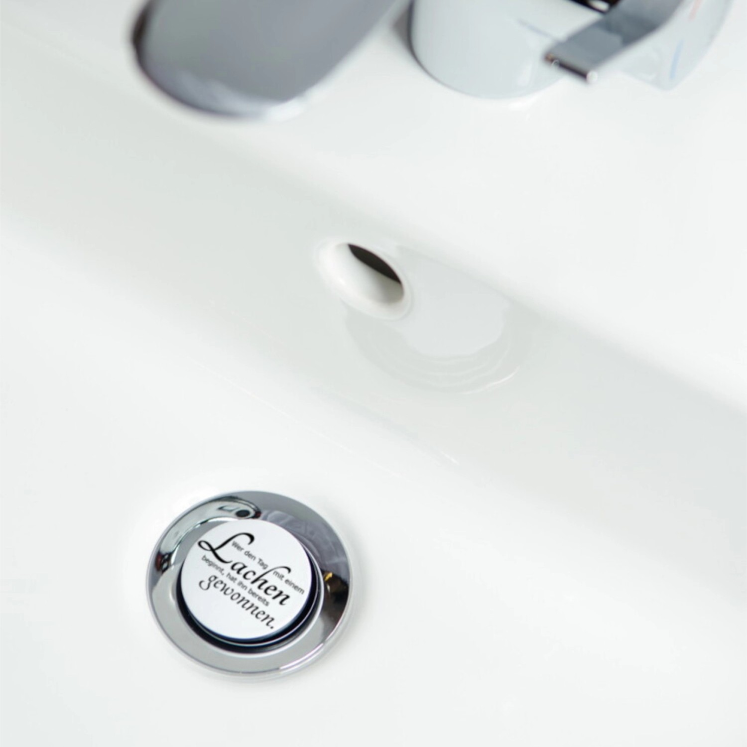 Sanilo Waschbeckenstöpsel mit dem Motiv 'Lachen' im weißen Waschbecken.