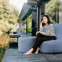 Frau sitzt auf blauem Sitting Point Hocker Outside (120 l) am Wasser. Bequemer Sitzsack für Outdoor & Indoor.