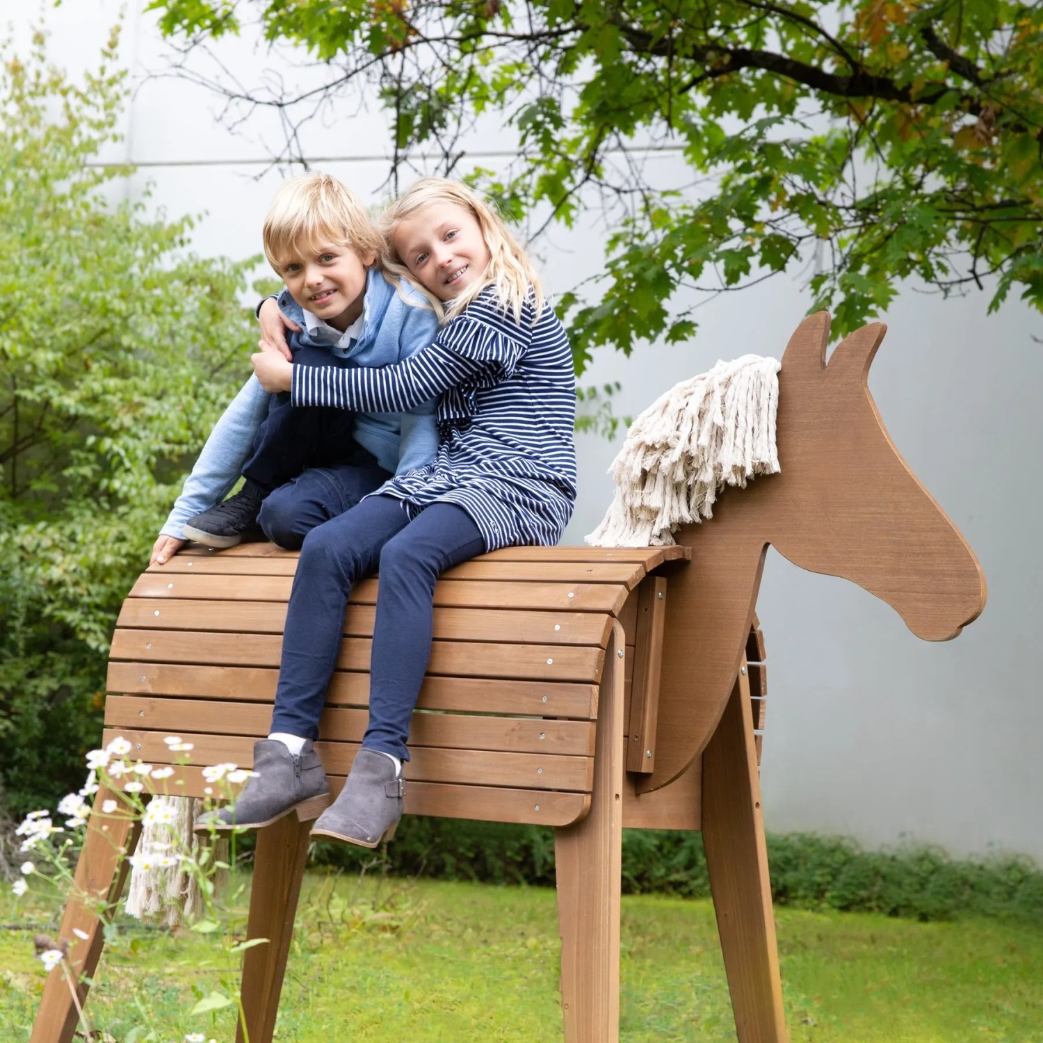 Zwei Kinder sitzen auf dem roba Spielpferd Sheddie aus Teakholz im Garten.