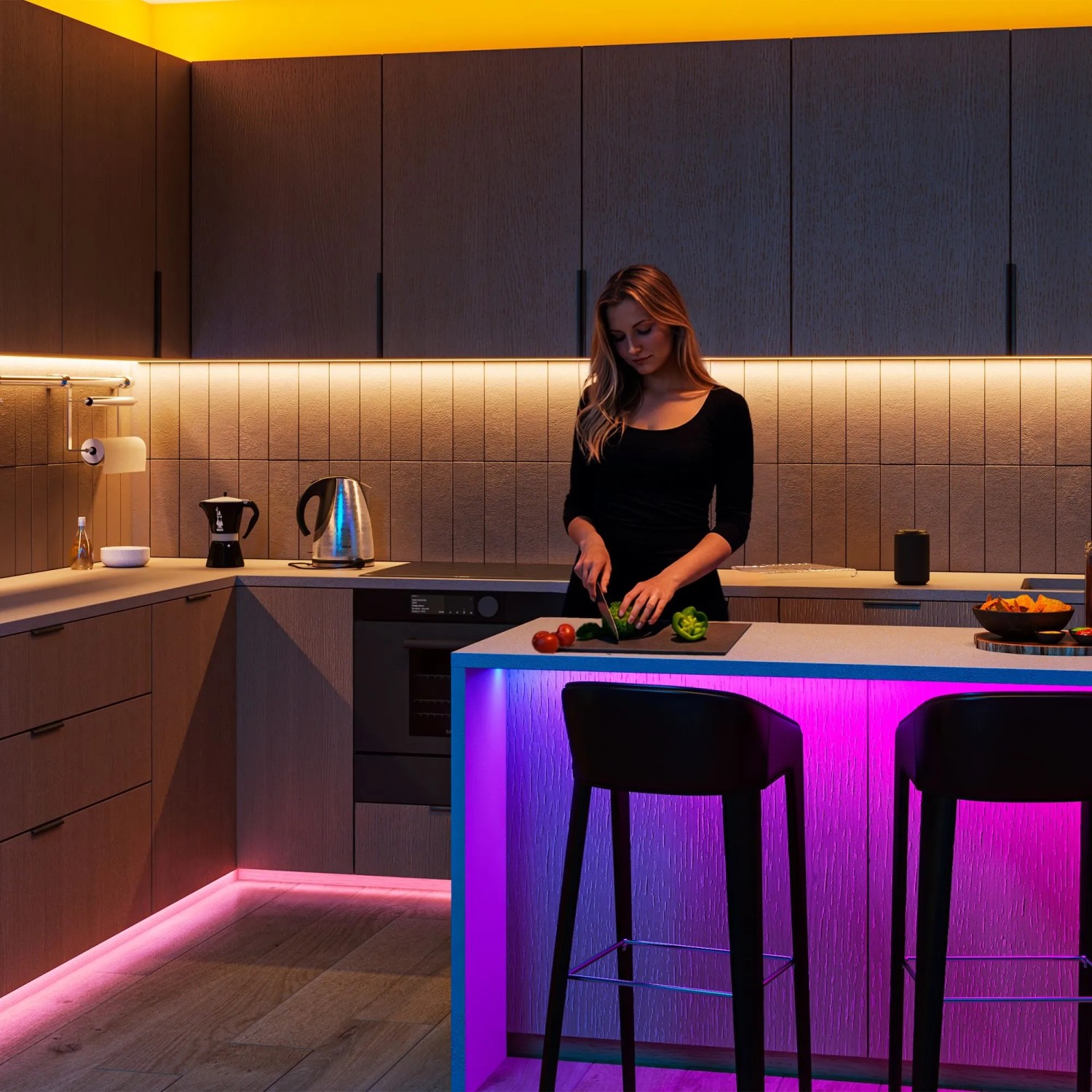 Moderne Küche mit Frau, beleuchtet von Philips Smart GU10 RGB LED-Licht. Farbige Akzente unter der Theke, warmweißes Arbeitslicht.