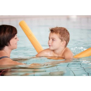 Kind mit gelber Poolnudel im Schwimmbad, von einer Frau begleitet. Vielseitige Schwimmhilfe aus Polyethylenschaum für Aqua-Fitness.