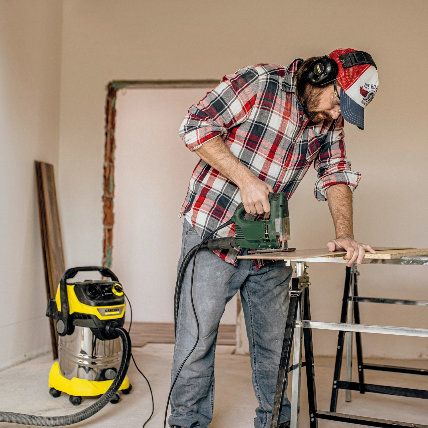 Mann sägt Holz mit Stichsäge, Kärcher Nass-Trockensauger WD 6 P S V-30/6/22/T im Hintergrund.