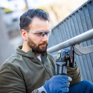 Mann trägt transparente LUX-TOOLS Schutzbrille beim Schleifen von Metall.