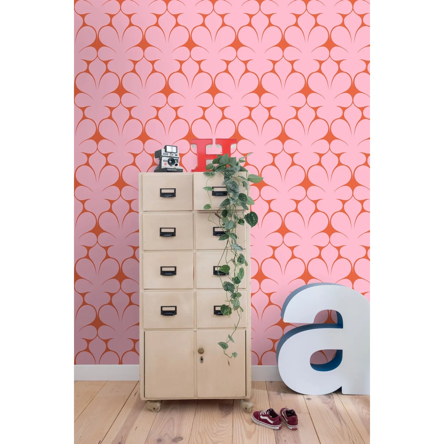 Rosa Vliestapete mit roten Retro-Ornamenten an einer Wand, die einen stilvollen Wohnraum dekoriert.
