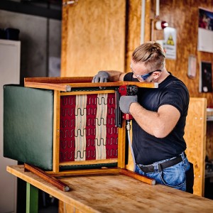 Mann arbeitet mit einem Druckluftnagler an einem Stuhl. Kompressor für Werkstatt.
