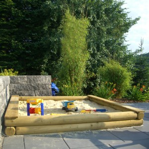 T & J Sandkasten Klaus aus Holz, 200x200 cm, mit Spielzeug im Garten.