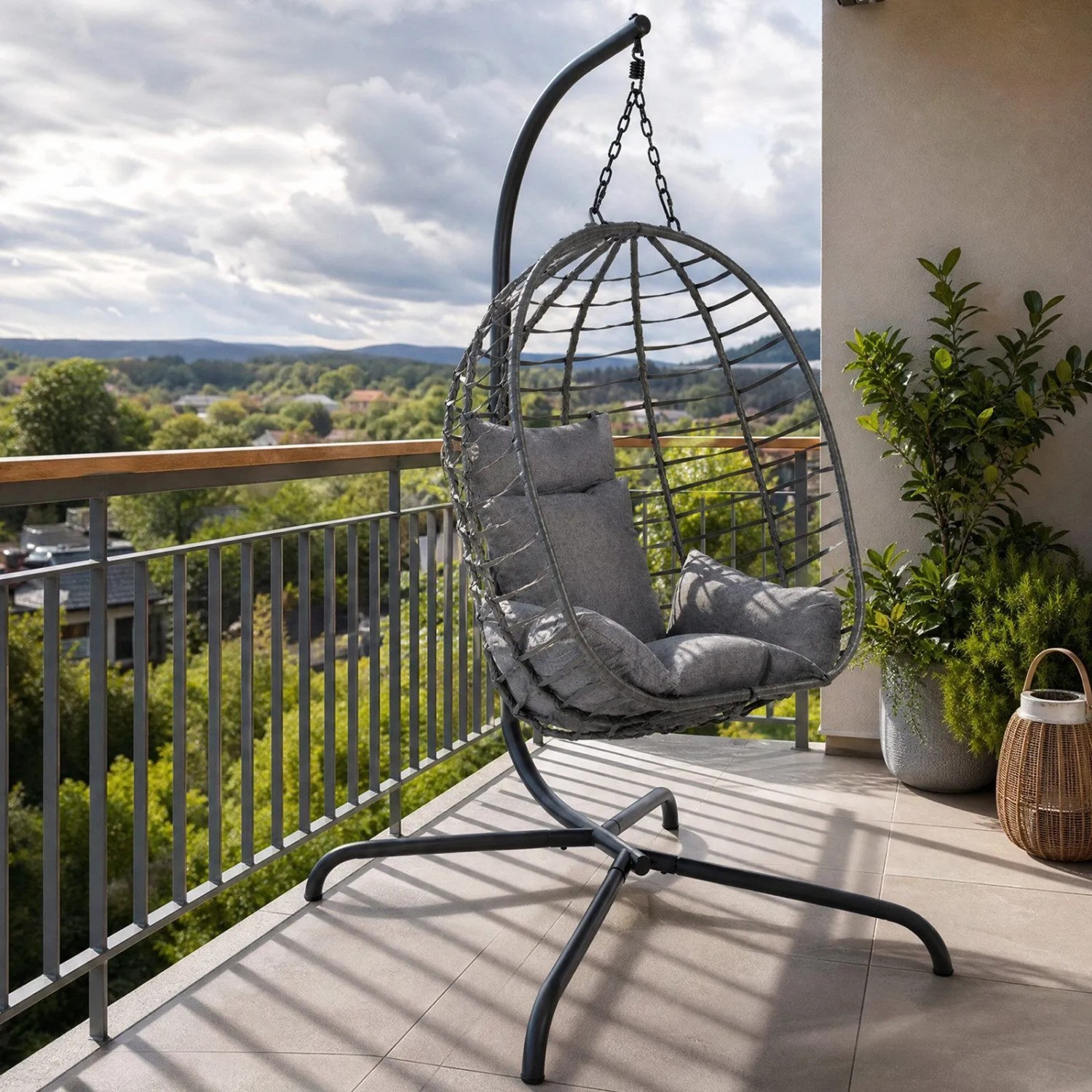 Grauer Hängesessel mit Rattan-Optik Korb, Gestell und Kissen auf Balkon. Bequemer Hängestuhl für Garten & Outdoor.