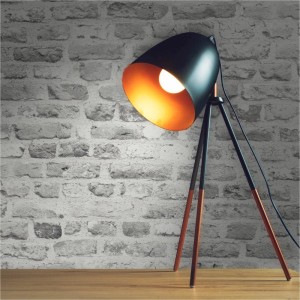 Tadessi Vliestapete mit grauer Ziegelsteinoptik, beleuchtet von einer schwarzen Stehlampe auf Holz. Dekorative Wandgestaltung.