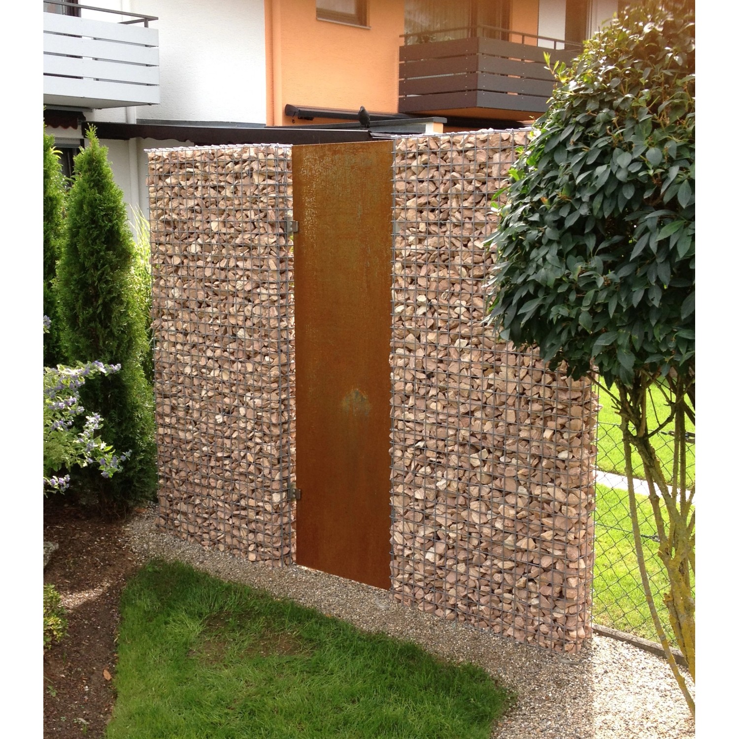 Gabiona Gabionenzaun (100x52x17 cm) mit Rost-Tür, gefüllt mit Steinen, im Garten.