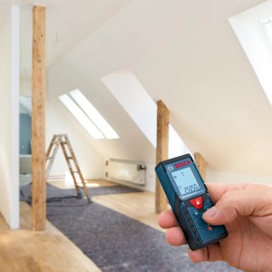 Bosch Professional GLM 40 Laser-Entfernungsmesser in Hand vor Dachgeschoss-Baustelle.