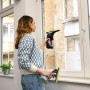 Frau reinigt Fenster mit Kärcher Akku-Fensterreiniger WV 1 Black Edition und Sprühflasche.