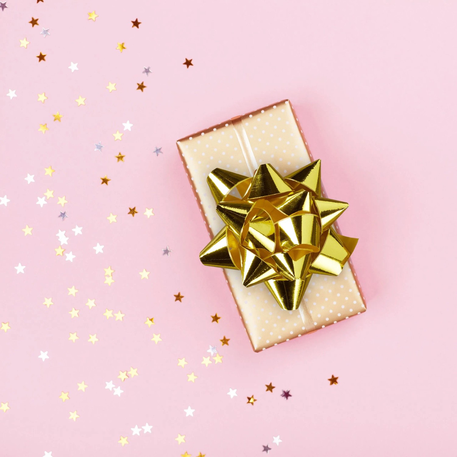 Glänzende goldene Zierschleife auf Geschenkbox, umgeben von Sternenkonfetti. Ideal für festliche Geschenkverpackungen.