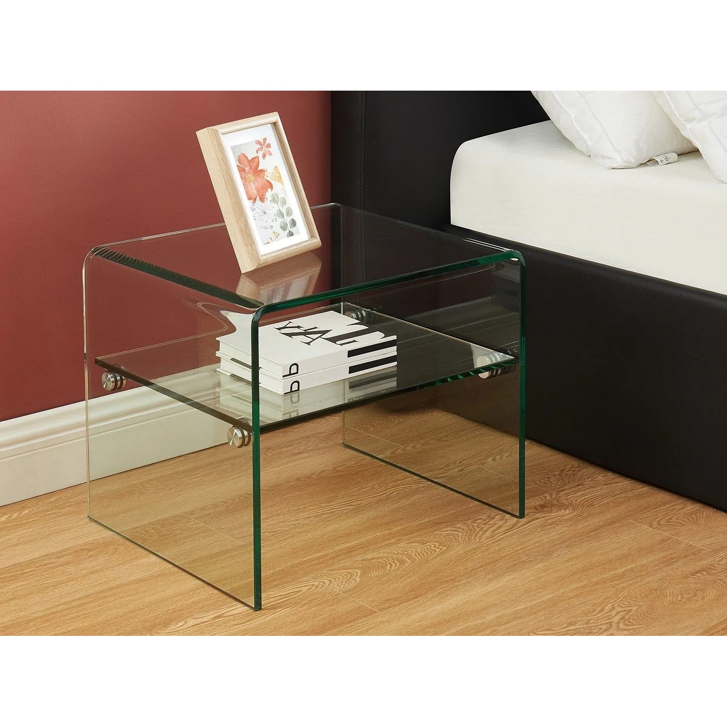 Transparenter Nachttisch Stileos aus Sicherheitsglas mit zwei Ablagen, 48 cm hoch, neben einem Bett.