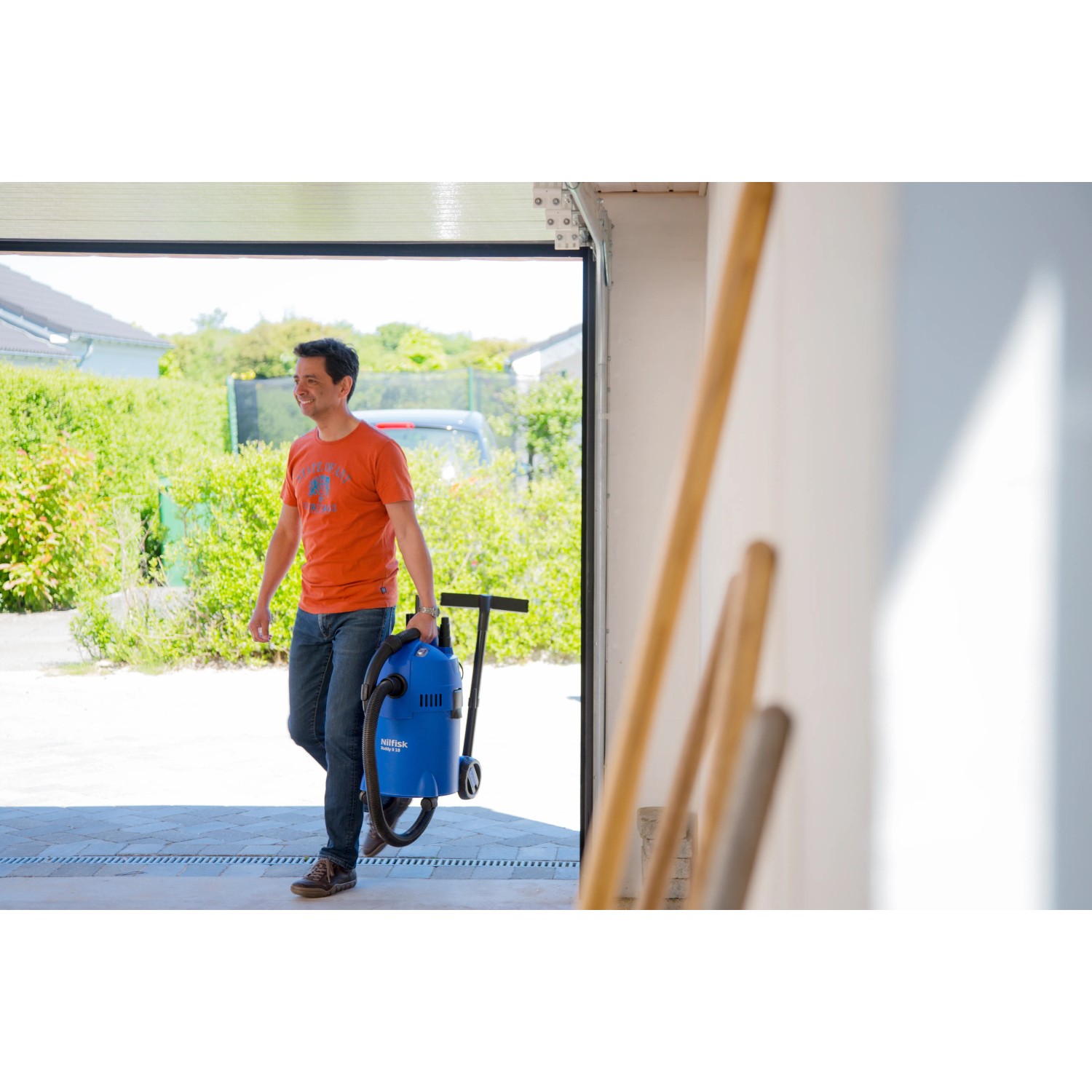 Mann trägt blauen Nilfisk Nass- und Trockensauger Buddy II 18 in Garage.