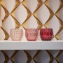 Nahaufnahme von drei Teelichthaltern in Rosa- und Rottönen vor einer goldenen Vliestapete mit 3D-Design.