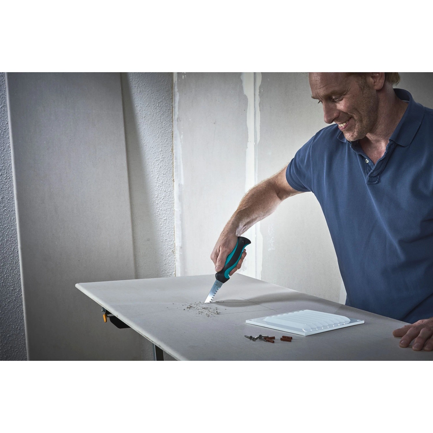 Mann sägt Gipskarton mit wolfcraft Handstichsäge, schwarzem 2-K-Griff. Ideal für präzise Ausschnitte im Trockenbau.