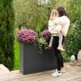 Westmann Pflanzkübel Talus XL, anthrazit, mit Blumen und Frau mit Kind im Garten.