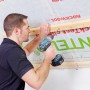 Mann befestigt Rockwool Formrock Untersparrendämmung (30mm) mit Schrauben an einer Holzkonstruktion.