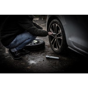 Mann wechselt Reifen am Auto mit Radkreuz. Ersatzrad liegt daneben.
