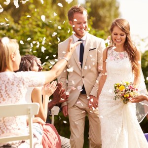 Glückliches Brautpaar auf Hochzeit, umgeben von fallenden weißen Rosenblättern. Gäste klatschen. Perfekt für Konfettikanone Rosenblätter.