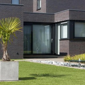 Karat Kunstrasen Windsor 25 mm auf Terrasse vor modernem Haus. Pflegeleichter, UV-beständiger Kunstrasenteppich.