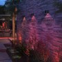 Philips Hue Resonate: Schwarze LED-Außenwandleuchten mit farbigem Lichtkegel an einer Steinwand.