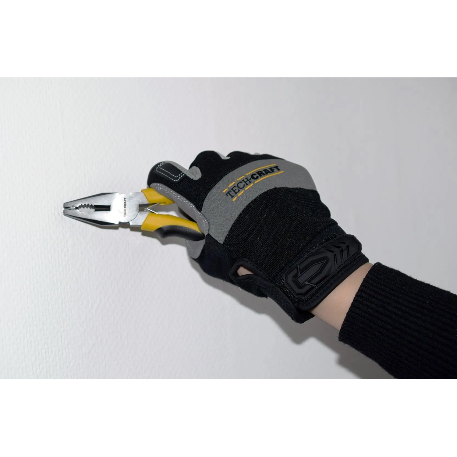 Hand mit TECH-CRAFT Handschuh hält Kombizange. Teil eines Werkzeugkoffers.