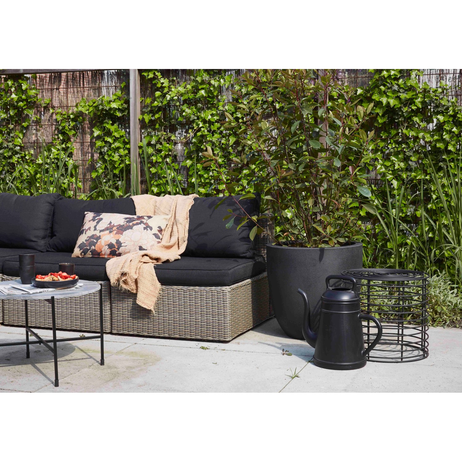 Schwarze Xala Gießkanne (12 l) neben Pflanzkübel im Garten.