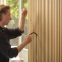 Mann installiert schwarzen OSRAM Acoustic LED-Streifen in Holz-Akustikpaneel. Zeigt die Montage des dimmbaren Streifens.