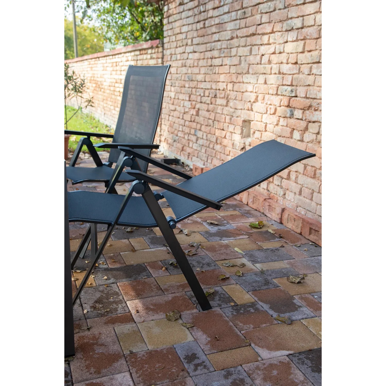 Anthrazitfarbener Acamp Klappsessel Urban aus Acatex-Gewebe und Aluminiumgestell vor einer Backsteinmauer.