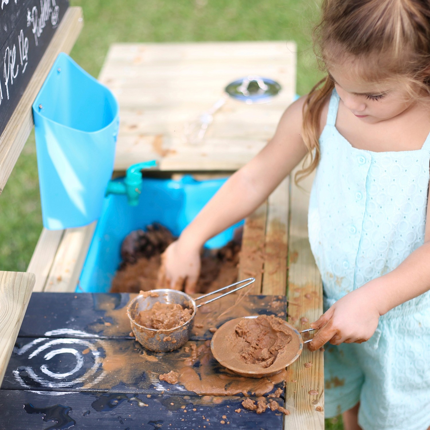Mädchen spielt mit Matsch in der TP Toys Kinderspielküche Deluxe aus Holz mit Zubehör.