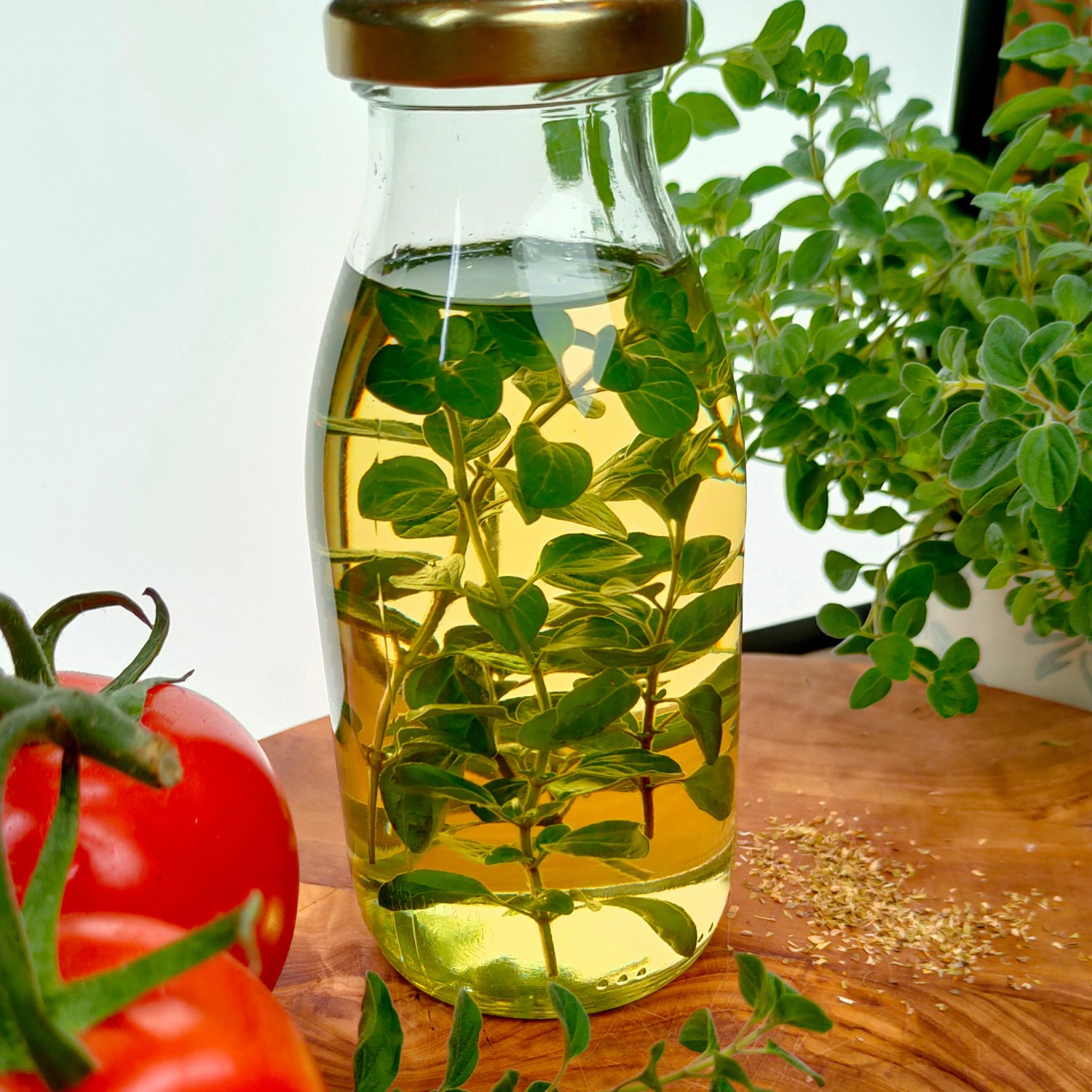 Bio-Majoran in Öl in Glasflasche, mit Tomaten und Majoranpflanze auf Holzbrett.