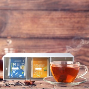 Relaxdays Tee Organizer mit 3 Fächern, weiß/transparent, neben einer Tasse Tee.