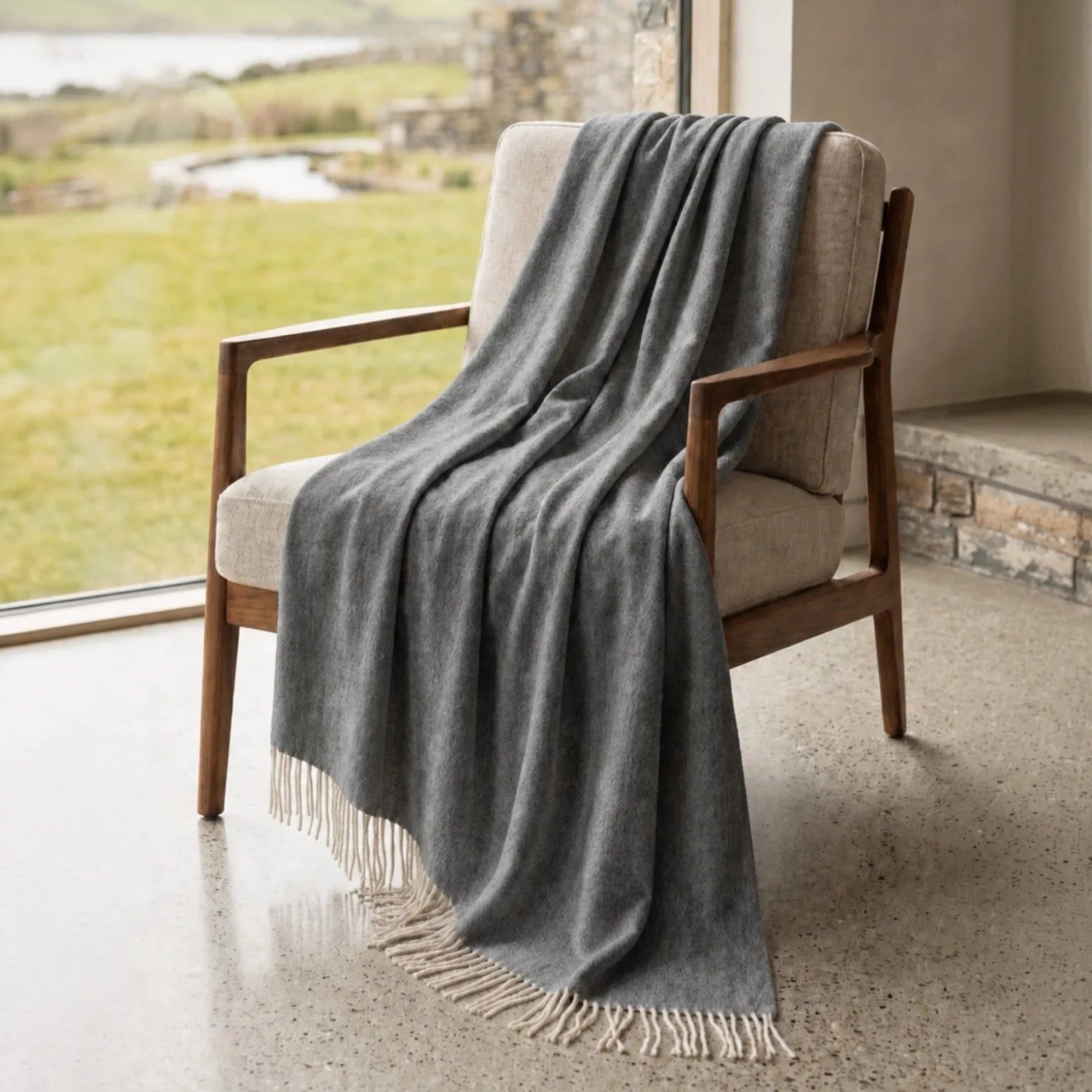Dunkelgraue Sofadecke aus Baumwoll-Mix mit Fransen, elegant über einem Sessel drapiert. Leichte Wohndecke für Sofa & Bett.